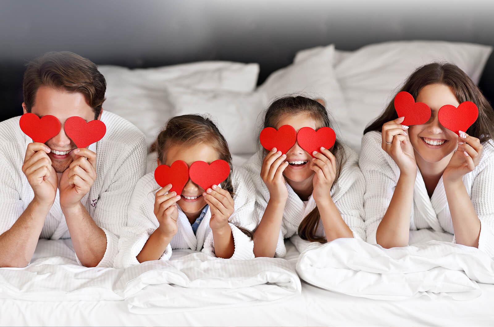 happy family lying on a bed hiding their eyes behind heart
