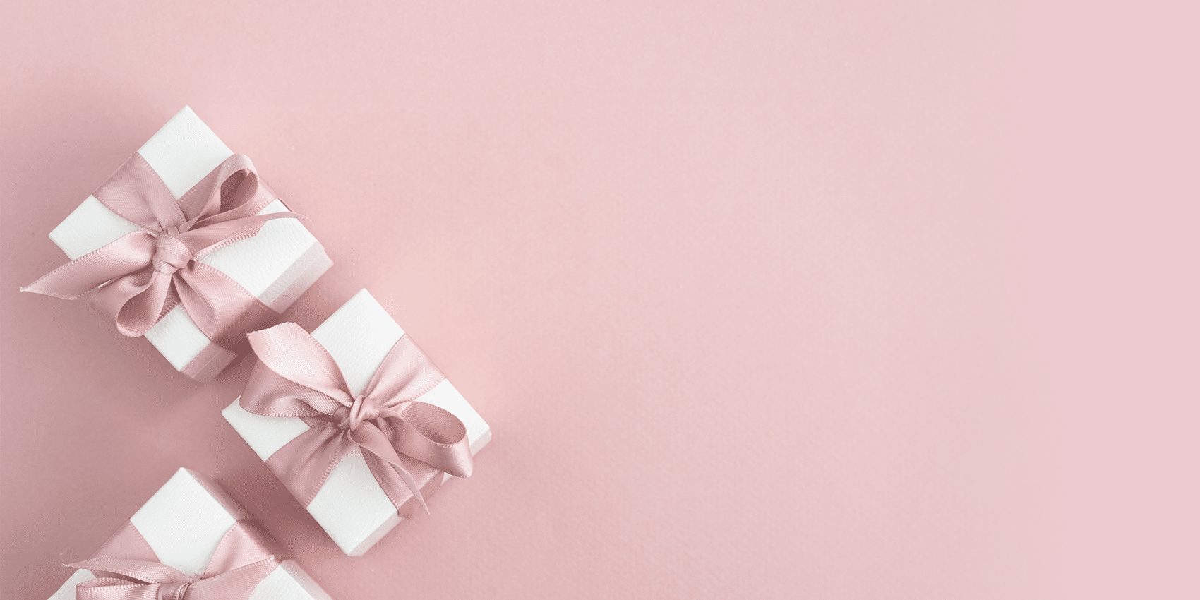3 white gift boxes with pink ribbon sitting on a pink surface