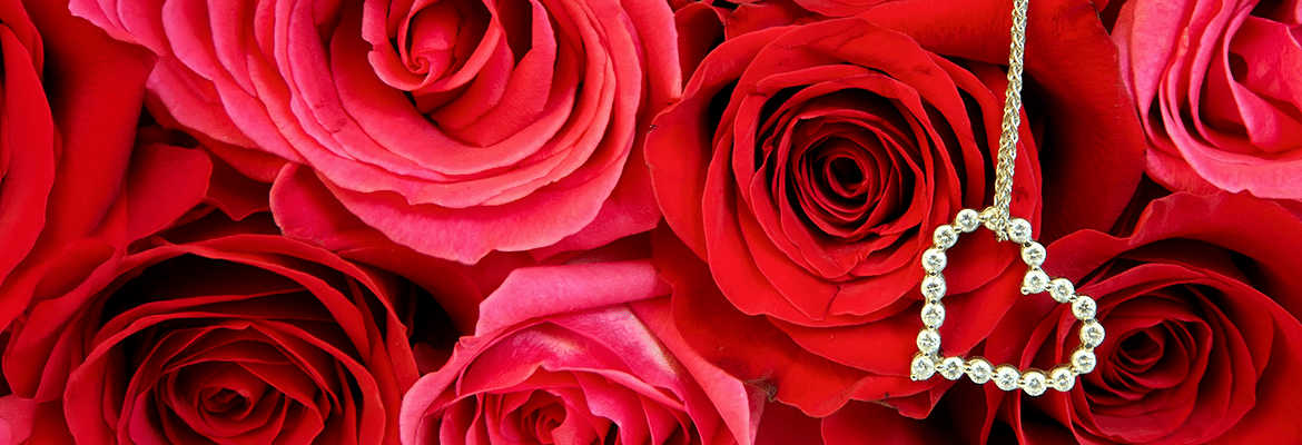 Yellow Gold heart shaped pendant with diamonds hanging in front of red rose background
